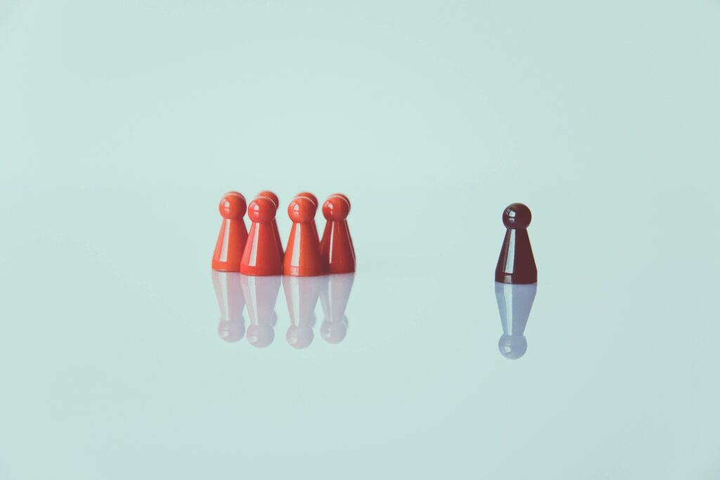 Red game pieces grouped with one isolated piece symbolizing social distancing on a reflective surface.